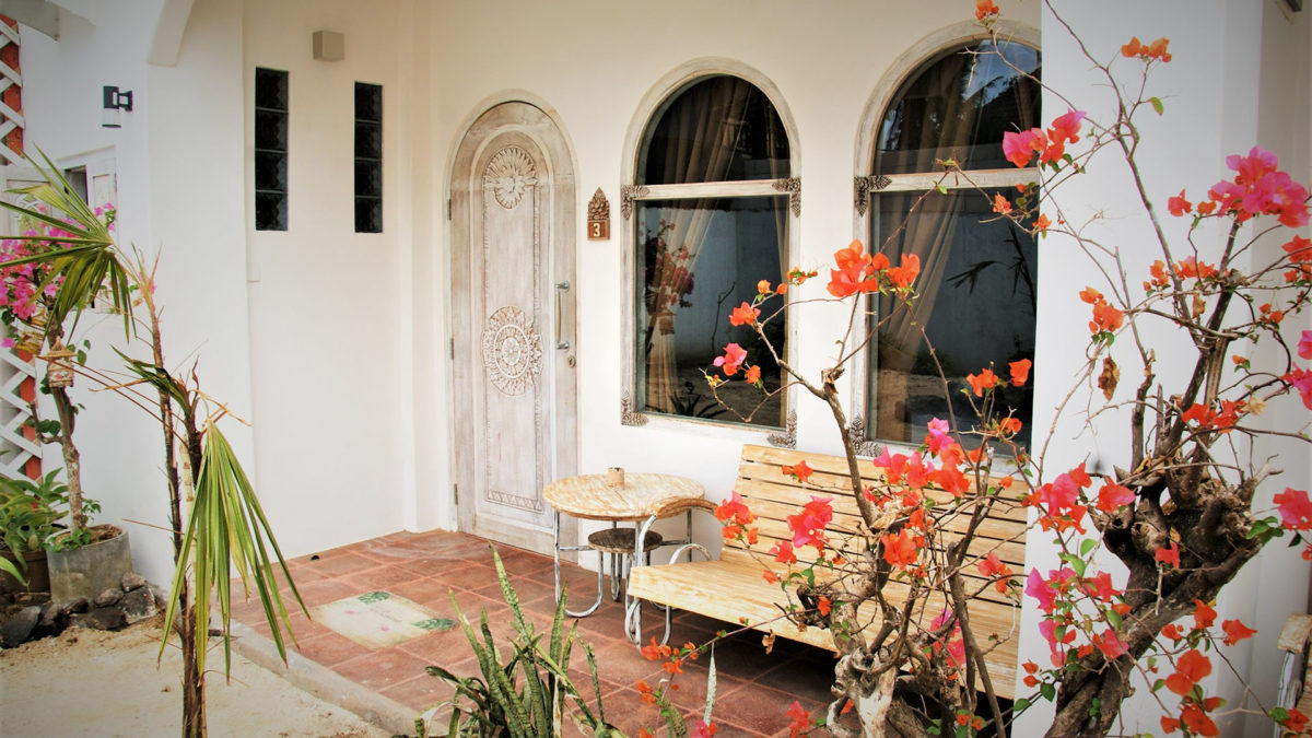 Isla Indah accommodation exterior with tropical flowers and shaded seating.